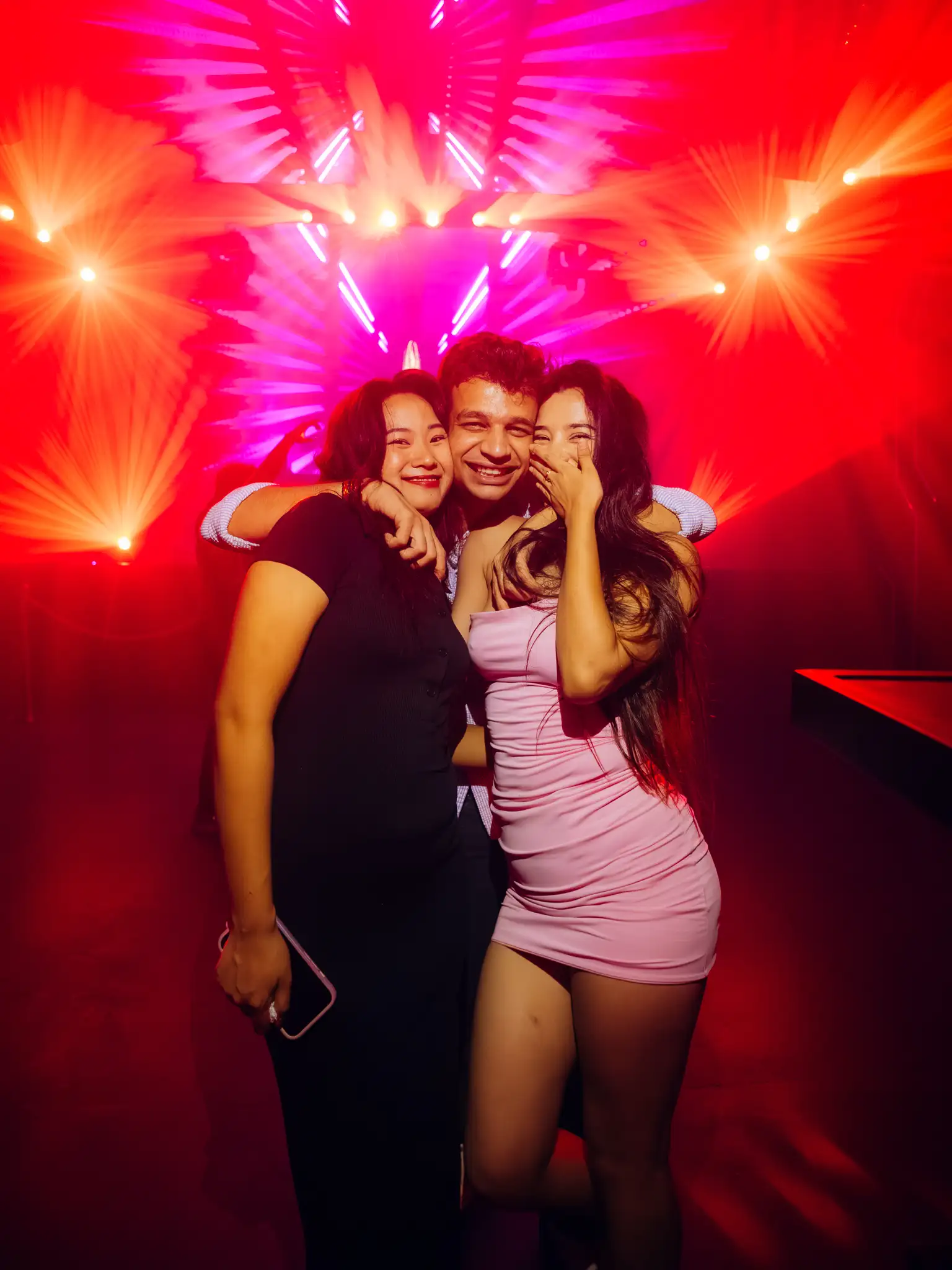 Three guests posing on the floor under red and magenta beam lighting